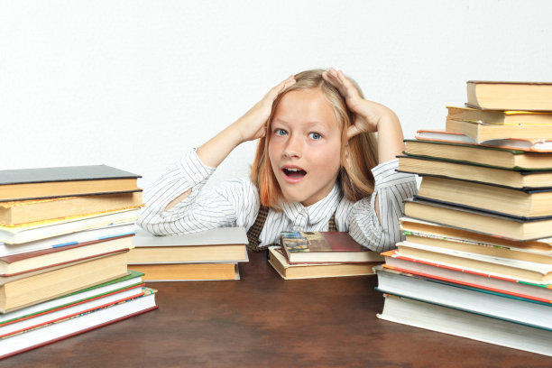 一个十几岁的女孩坐在一张桌子上，累了，在书和做她的家庭作业。用手托住他的头。孤立的背景。图片下载