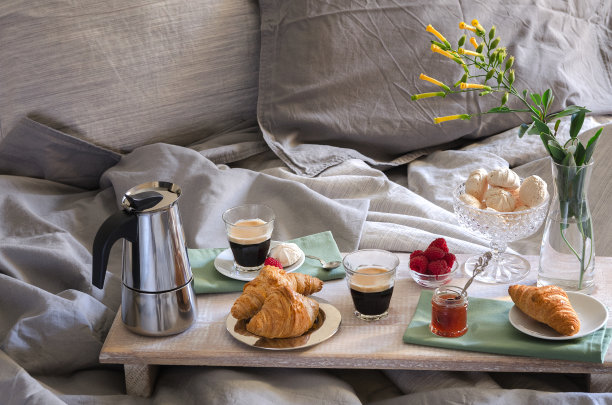 双人床上浪漫早餐。咖啡机和咖啡杯，羊角面包，果酱，覆盆子蛋白酥皮和木托盘上的花。浪漫的早安风景图片下载