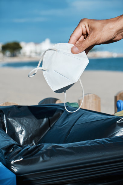 一名男子将用过的面具扔向海滩上的垃圾桶图片下载