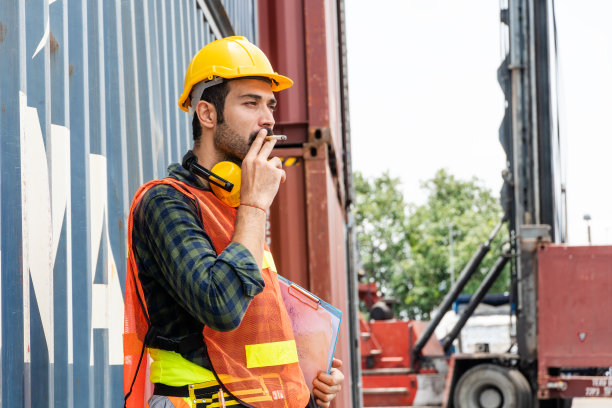 拍摄一名建筑工人在集装箱仓库工地休息时抽烟的照片。工业和工厂的概念背景与复制空间图片下载