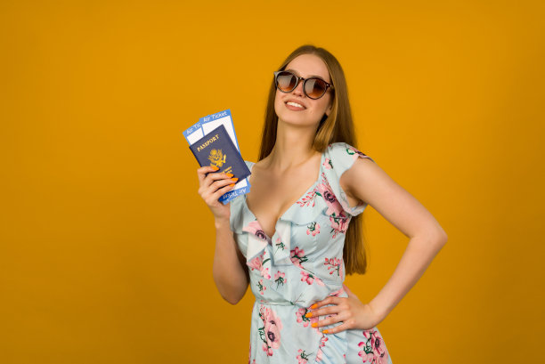 一名快乐的年轻女子身穿蓝色连衣裙，戴着太阳镜，手里拿着黄底护照的机票。图片下载