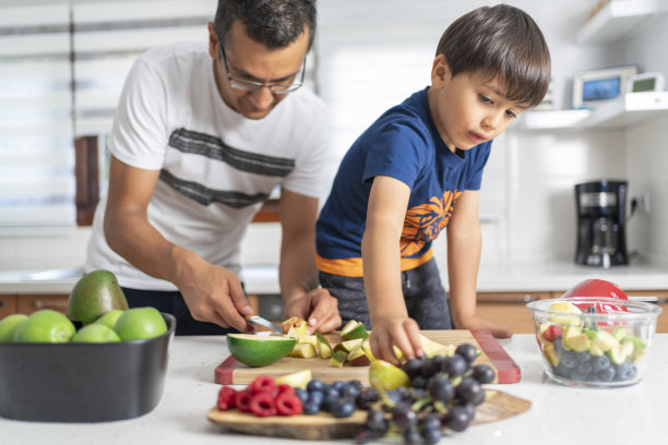 年轻的父亲和他可爱的小儿子在厨房一边切水果一边准备健康的奶昔图片下载