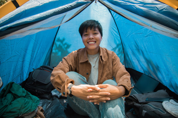 微笑的亚洲男子坐在室内的帐篷，一个背包，手机，笔记本电脑，行李放松露营独自度假的早晨图片下载
