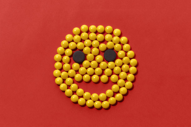 俯视图黄色和黑色药丸躺在微笑的形状，脸孤立在红色背景。保健和治疗概念。图片下载