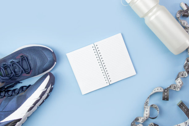 运动平面布局。健身配件运动鞋，瓶子和打开笔记本书写在一个蓝色的背景。运动规划图片下载