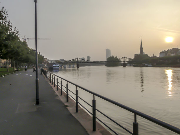 河边夕阳西下，一些建筑物作为背景，人们沿着河边的道路慢跑。图片下载