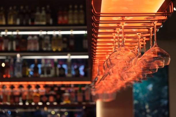 看看晚上挂在酒吧里的一排空酒杯。架子上散焦的酒瓶图片下载