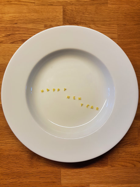“新年快乐”由可食用的字母组成。以木为背景的盘子上的字母形式的意大利面。图片下载