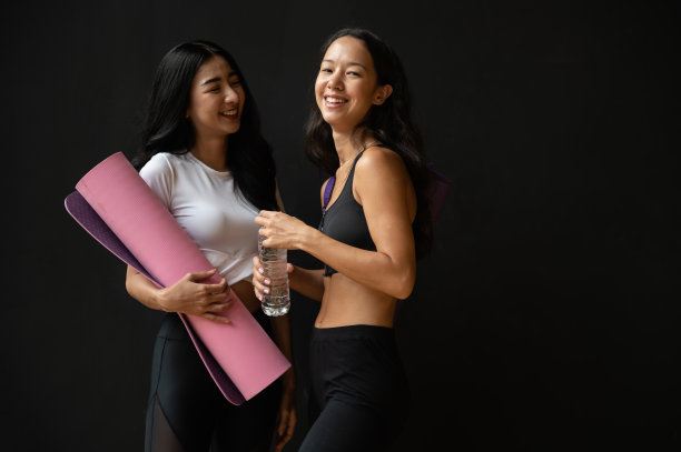 两个年轻迷人的女性朋友看起来完美和健康的谈话后，休息与黑色背景。两位女性在健身房里从锻炼中得到了放松和快乐。图片下载