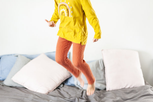 一个穿着黄色和橙色衣服的小女孩在床上跳图片下载