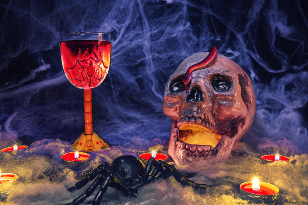 万圣节装饰品。一个人的头骨和一条蛇，旁边站着一杯用蜘蛛和头骨装饰的红酒图片下载