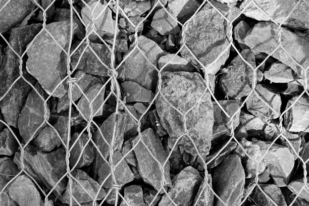 砂砾覆盖着金属丝的地面，背景照片纹理，俯视图。金属格栅下碎石制成的滑坡防护图片下载