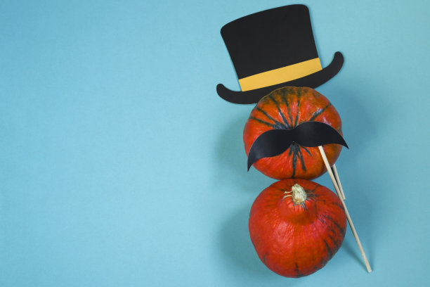 蓝色背景上的南瓜，黑色的纸帽子，八字胡，平躺着。大气的形象。秋天的明信片。万圣节快乐。副本的空间。图片下载