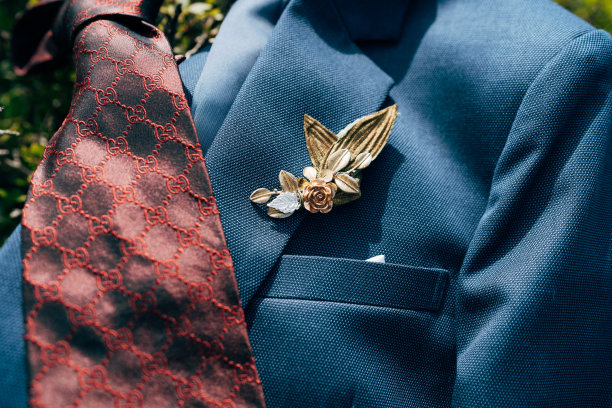一个暗红色图案的领带的特写和新郎在一件蓝色夹克上的胸花。图片下载
