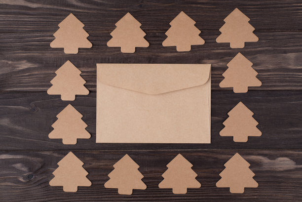 上面的头顶视图平铺的照片，圣诞树形状的纸装饰，使一个广场与信封在中心孤立的木制背景与copyspace图片下载