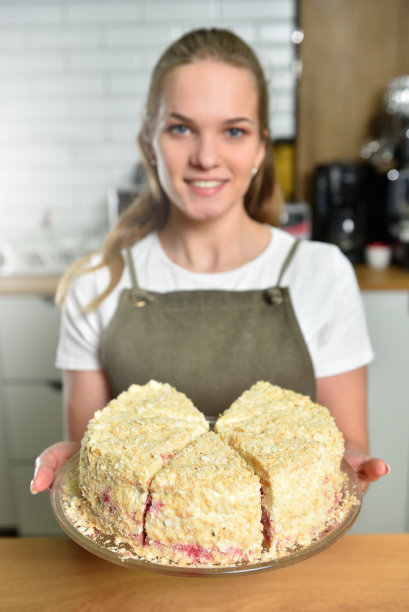 一个年轻的咖啡师在咖啡店拿着一个新鲜准备的蛋糕，微笑着。小生意和吃糖果的概念图片下载