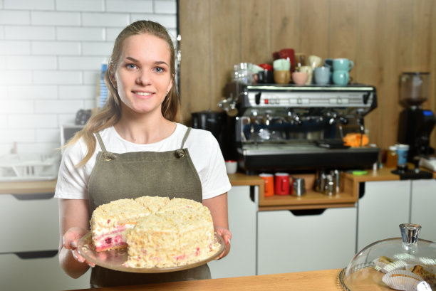 一个年轻的咖啡师在咖啡店拿着一个新鲜准备的蛋糕，微笑着。小生意和吃糖果的概念图片下载