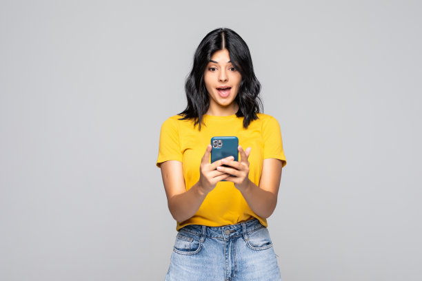 输入信息给朋友。迷人的年轻女子拿着智能手机，看着它微笑，而站在灰色的背景图片下载