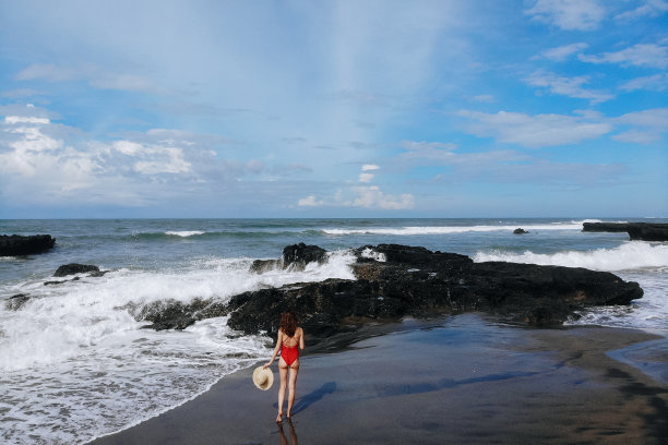 航拍的女人在红色比基尼和草帽在手走在海洋海滩与黑沙。在巴厘岛度假。图片来自无人机图片下载