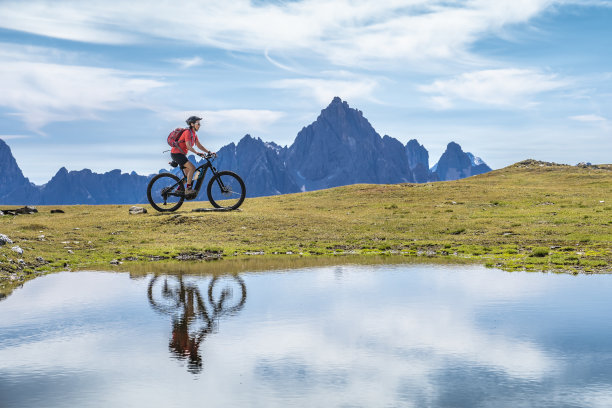 骑着电动山地车的好女人在山湖里倒影图片下载
