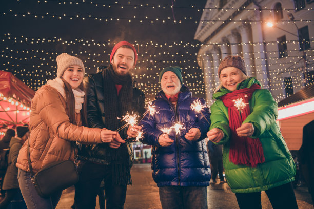 全家四人的照片，圣诞聚会，举行烟花，等待时钟的钟声，在新年的最后几分钟，外套，帽子，围巾，外套，晚上，街道照明户外图片下载