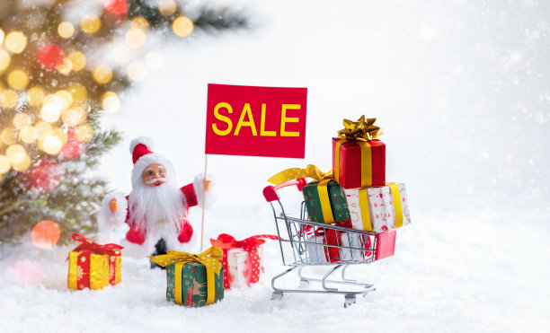 迷你购物手推车和礼物盒在雪白的背景与圣诞老人对云杉树枝散焦闪烁的灯。圣诞促销的概念。图片下载