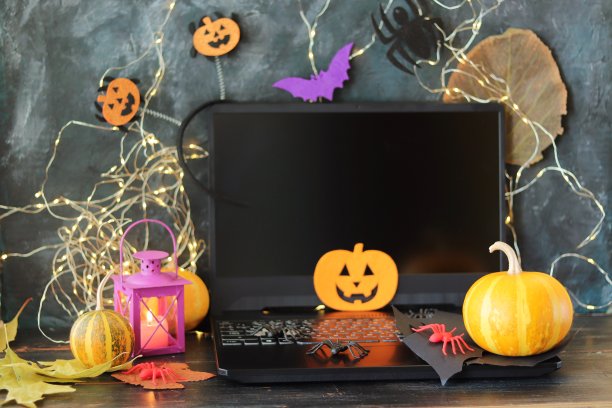 万圣节快乐，南瓜，可怕的脸雕刻在秋叶上，神秘的装饰和一个灯笼与燃烧的蜡烛，笔记本电脑在黑色的背景图片下载