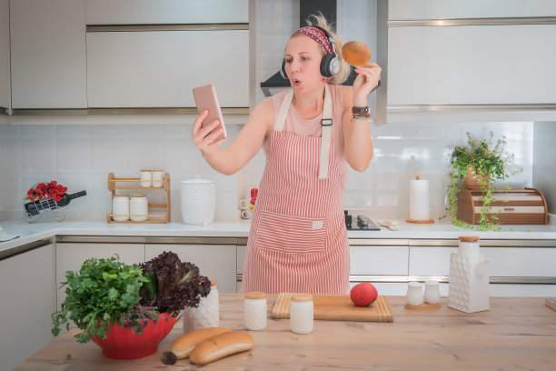 快乐的女人在厨房用智能手机自拍。图片下载