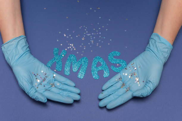 双手戴医用手套，蓝色背景。在手中闪烁着小星星。铭文圣诞节。圣诞和新年贺卡的概念。俯视图照片，复制空间。图片下载