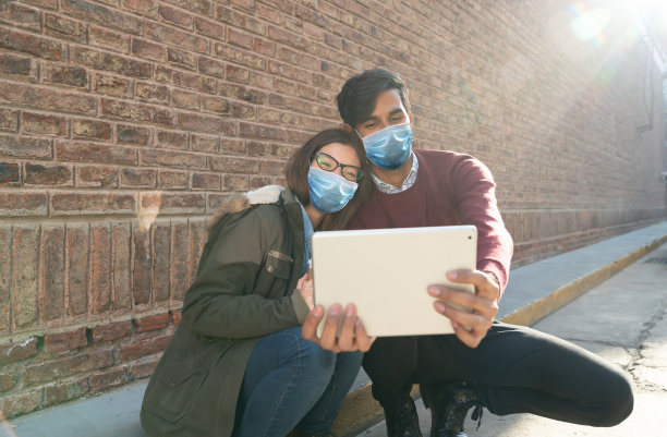 这是一对夫妇用平板电脑自拍的照片，平板电脑的背面是一座砖砌建筑。COVID概念图片下载