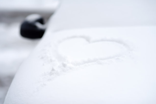 画在汽车引擎盖上的雪心。一整夜的暴风雪过后，汽车上覆盖了新雪。图片下载