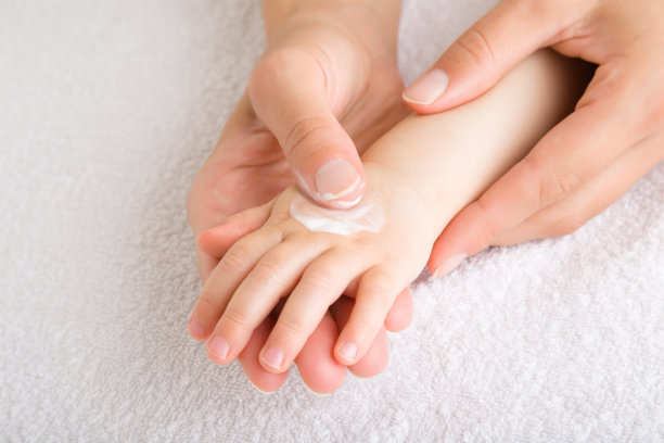 年轻的妈妈用手指将润肤霜涂在宝宝的手上。关爱孩子洁净柔软的身体肌肤。特写镜头。图片下载