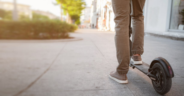 男子骑黑色电动踏板车在日落的城市景观的特写图片下载