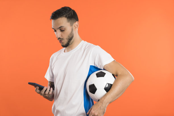 激动的足球运动员或球迷腋下夹着球看他的智能手机惊讶。广告的概念图片下载