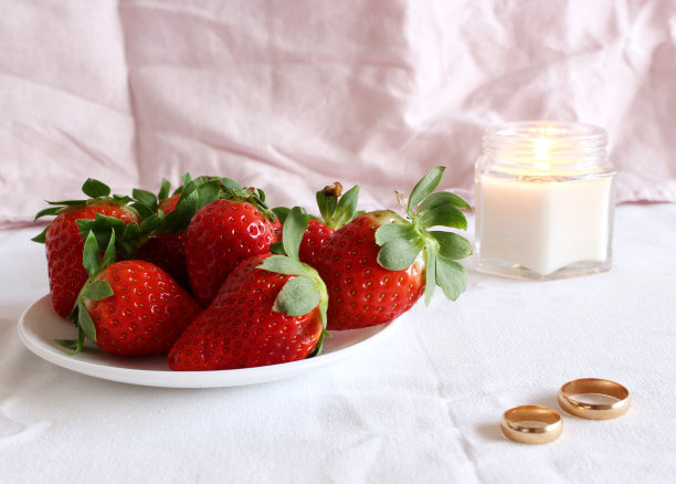 明亮的婚礼场景，瓷盘上的新鲜草莓和婚礼戒指的白色背景。女性风格的库存照片。图片下载
