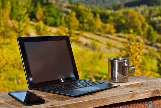 旧的划痕马克杯，智能手机和笔记本电脑的自然背景。闪亮的不锈钢杯放在木板上。把手机放在笔记本电脑旁边。图片下载