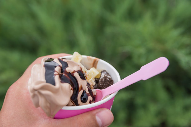 特写照片的纸杯与冰淇淋在男人的手在绿色的背景在公园。咖啡冰淇淋配蜜饯水果和巧克力饼干。图片下载