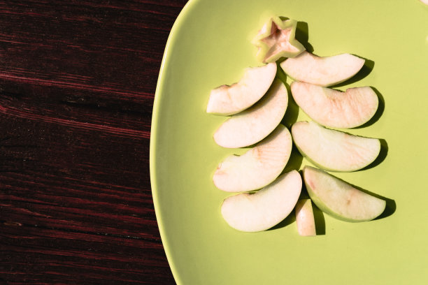 适合全家人和孩子的圣诞甜点。美味健康的自助餐。一棵以红木为背景的绿色盘子上的绿色苹果片制成的圣诞树。图片下载