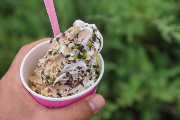 特写照片的纸杯与冰淇淋在男人的手在绿色的背景在公园。提拉米苏冰淇淋覆盖着碎开心果和苦巧克力。图片下载