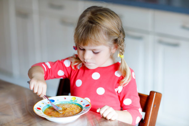可爱的小蹒跚学步的女孩在厨房吃新鲜煮熟的蔬菜汤。快乐的孩子午餐或晚餐吃健康的食物。孩子学习。家庭，托儿所，幼儿园或日托所图片下载