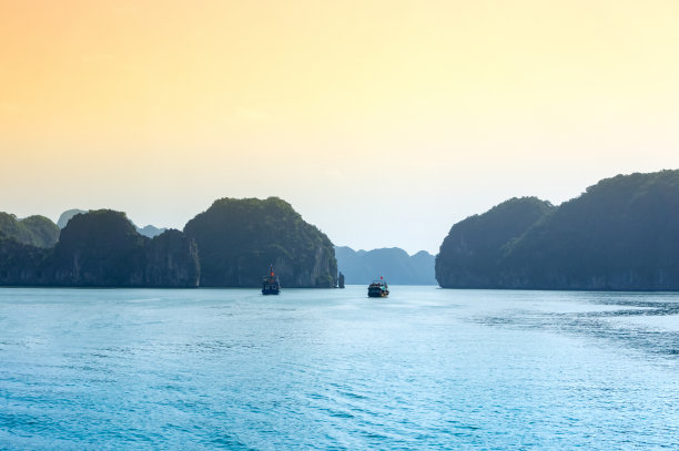 日落和黎明附近的岩石岛，下龙湾，越南，东南亚。舢板游船到下龙湾。受欢迎的地标，越南著名的目的地。两艘船驶过地平线图片下载