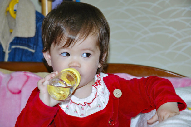 亚洲女婴穿红色衣服喝奶瓶里的水。从侧面看图片下载