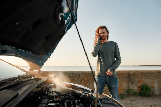 一名年轻男子站在他的破车旁边，用智能手机寻求帮助图片下载