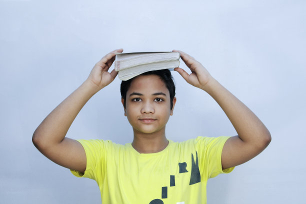学生，孩子，一本书在他的头上，孤立在白色的背景图片下载