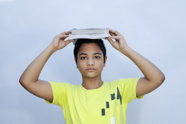 学生，孩子，一本书在他的头上，孤立在白色的背景图片下载