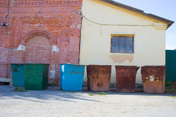 在一个阳光明媚的夏日里，彩色的旧空垃圾桶映衬着一座砖房和一座用黄色灰泥砌成的建筑。图片下载