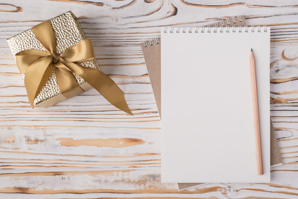 上面的俯视视图平放一张空白笔记本铅笔和金色礼物盒的照片孤立在与copyspace的浅色木制背景上图片下载