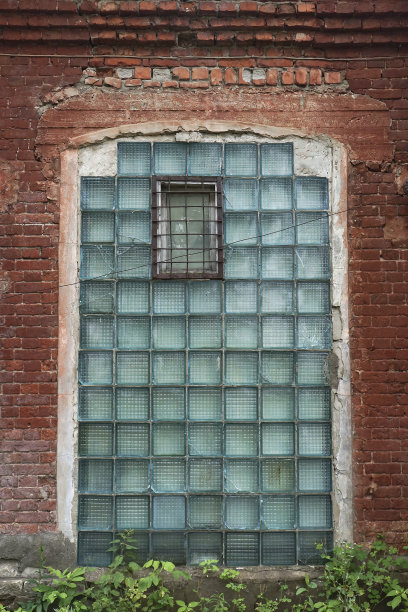 红色的砖墙是一个废弃的工厂，有一个大窗户和蓝绿色的浮雕玻璃块关闭图片下载