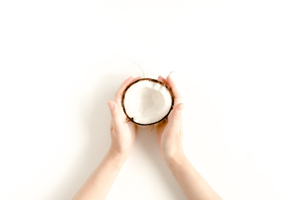 女人的手拿着一半椰子在白色的背景。平躺，俯视图图片下载