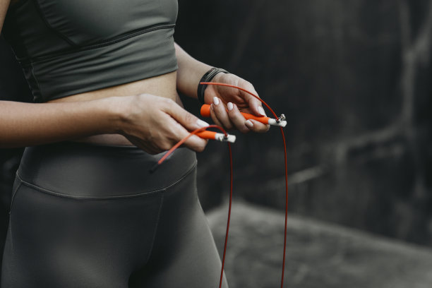 跳绳锻炼:一个健康女人的手拿着一个橙色的速度绳子图片下载